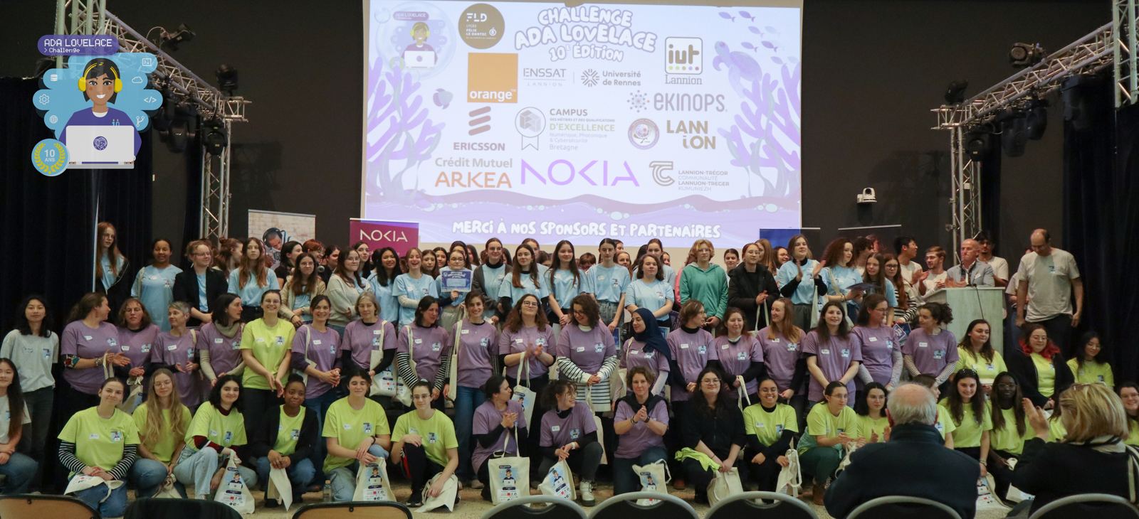 Photo de groupe de l'édition 2025 à Lannion : les participantes, les tutrices, les jurées et l'équipe d'organisation, devant l'écran aux couleurs du challenge